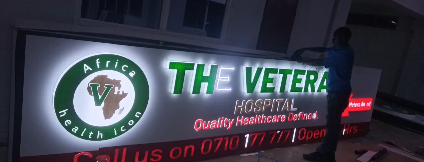 Wide illuminated fascia light box being fitted above a hospital entrance